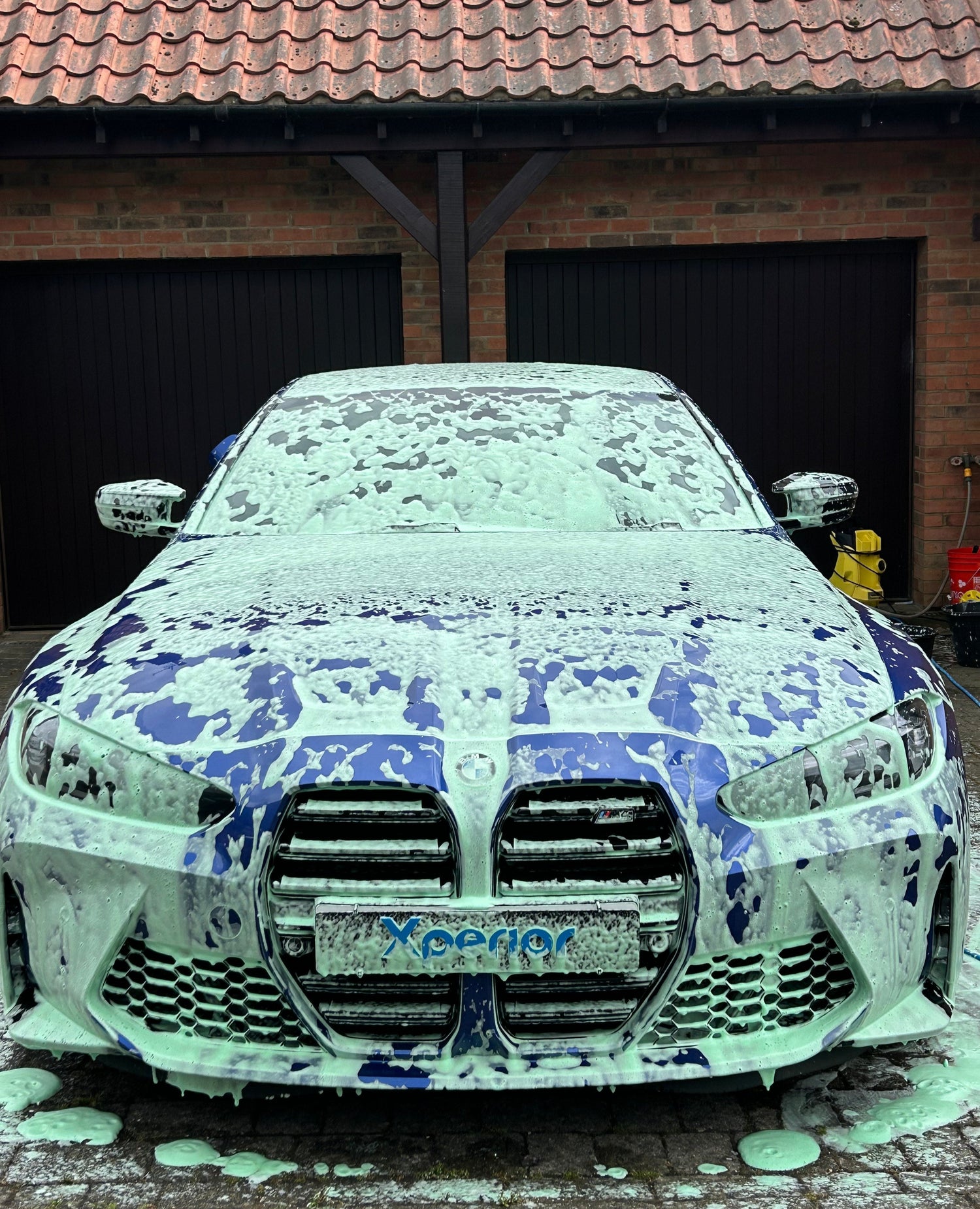 Blue BMW M4 coated in vibrant green snow foam during pre-wash by Xperior Detailing in Northampton