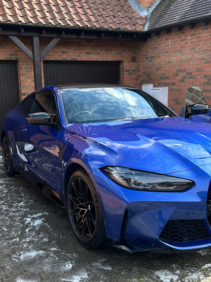 Blue sports car parked on a driveway next to a brick building after a ceramic coating looking glossy